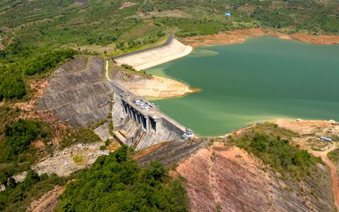 Aerial view of a dam and green reservoir in hilly, forested terrain
