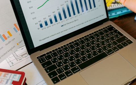 Laptop showing performance charts on a desk covered with printed reports