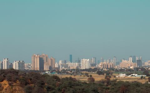 Gurugram skyline in Delhi-NCR beyond the green Aravalli scrub and a curving road