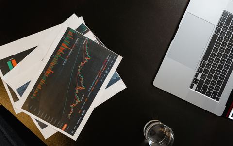 Printed performance charts and a laptop on a dark desk