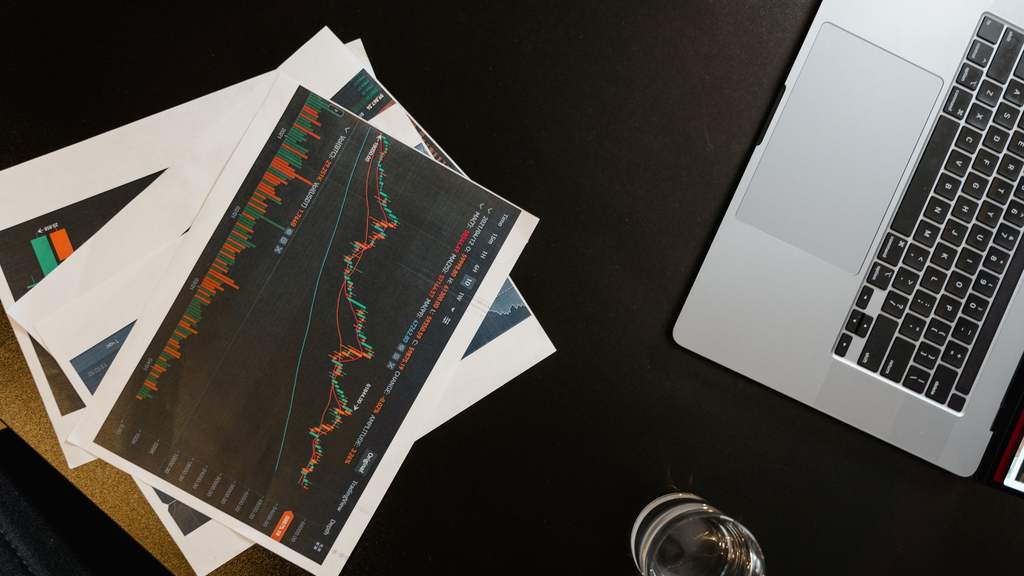 Printed performance charts and a laptop on a dark desk
