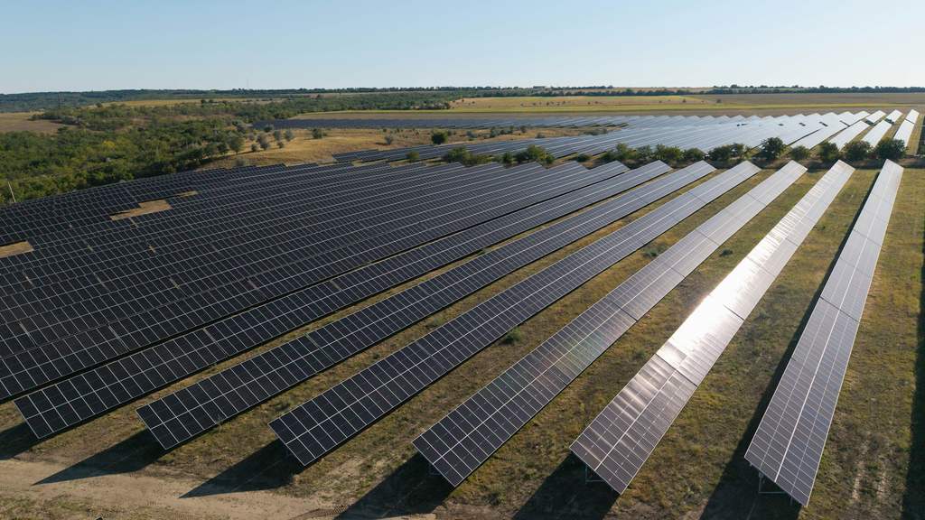 Aerial view of long rows of solar panels across a rural landscape