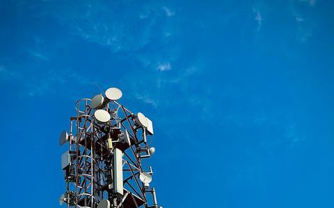 Telecom tower with mobile antennas and microwave dishes against a deep blue sky in Punjab, India