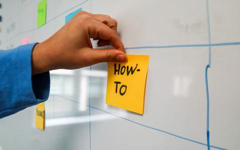 Hand placing a yellow sticky note on a whiteboard during a workshop